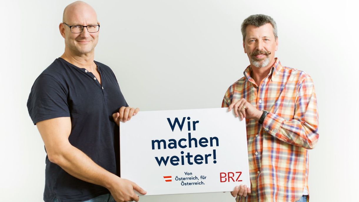 Zwei BRZ-Mitarbeiter halten in Schild mit der Auschrift "Wir machen weiter! - Von Österriech, fur Österreich."