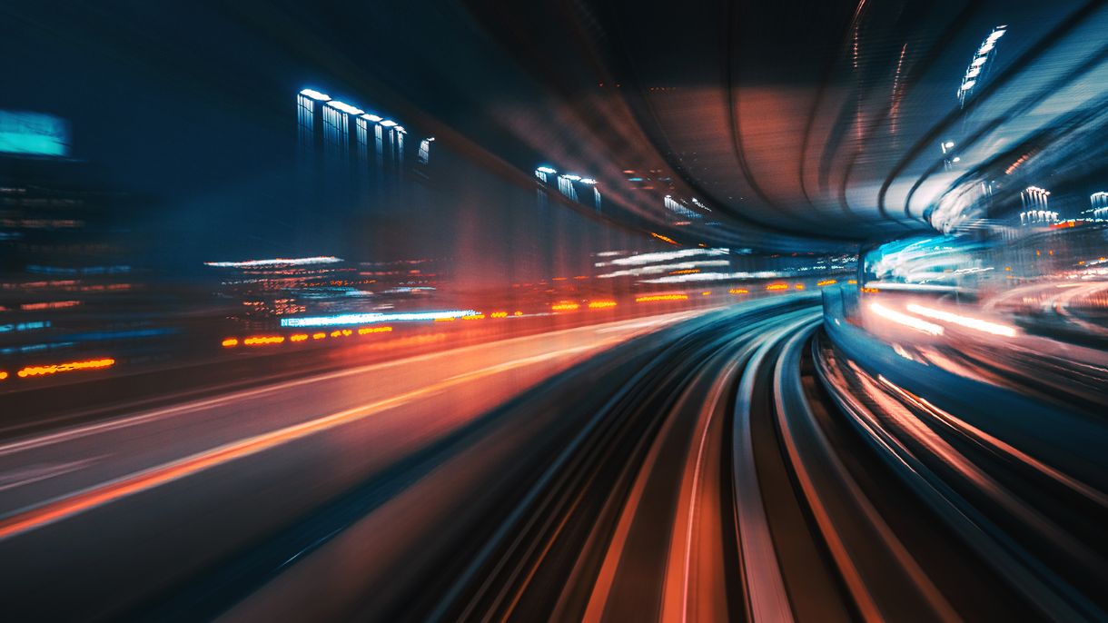 20_zug_(c)istock_Nikada, @iStock.com/Nikada Verschwommene Stadtlichter auf einer nächtlichen Schienenfahrt.