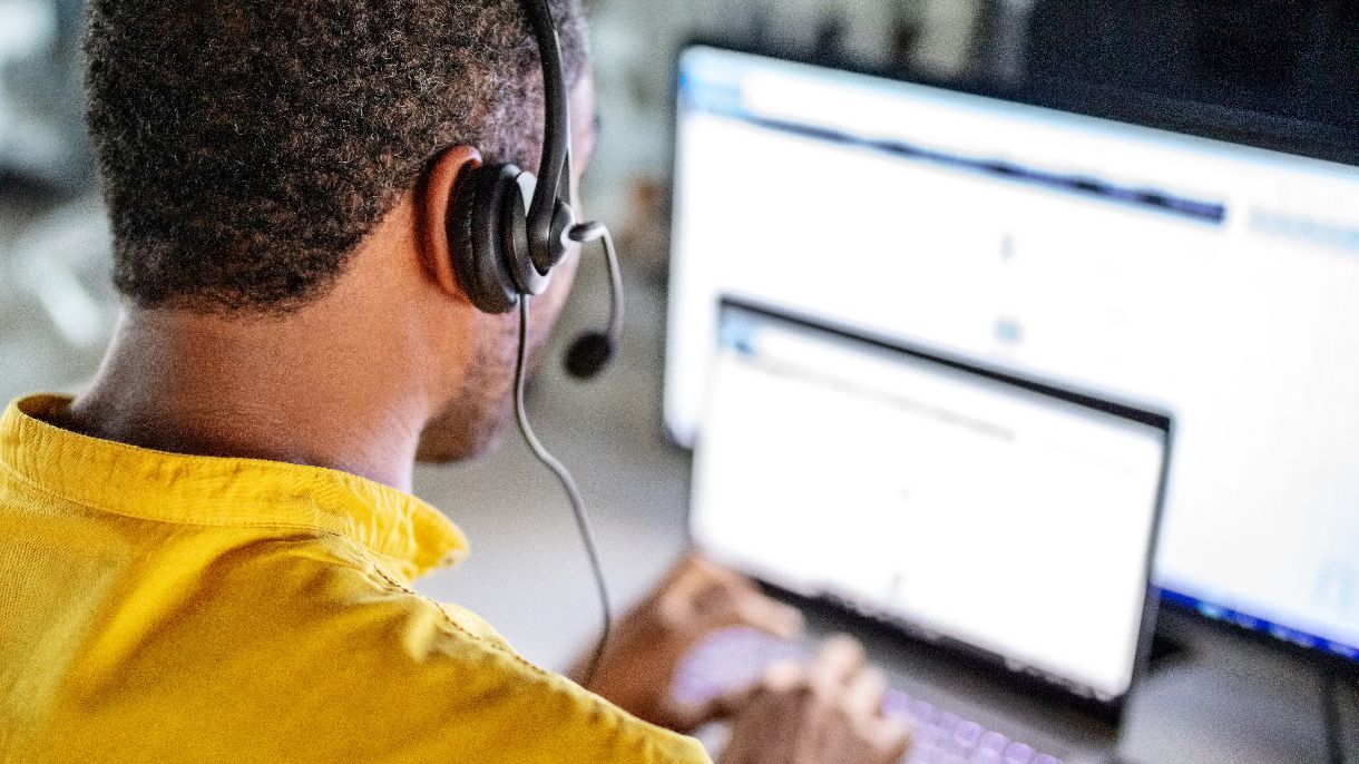 Service-Center Mitarbeiter von hinten mit Headset tippt am Laptop