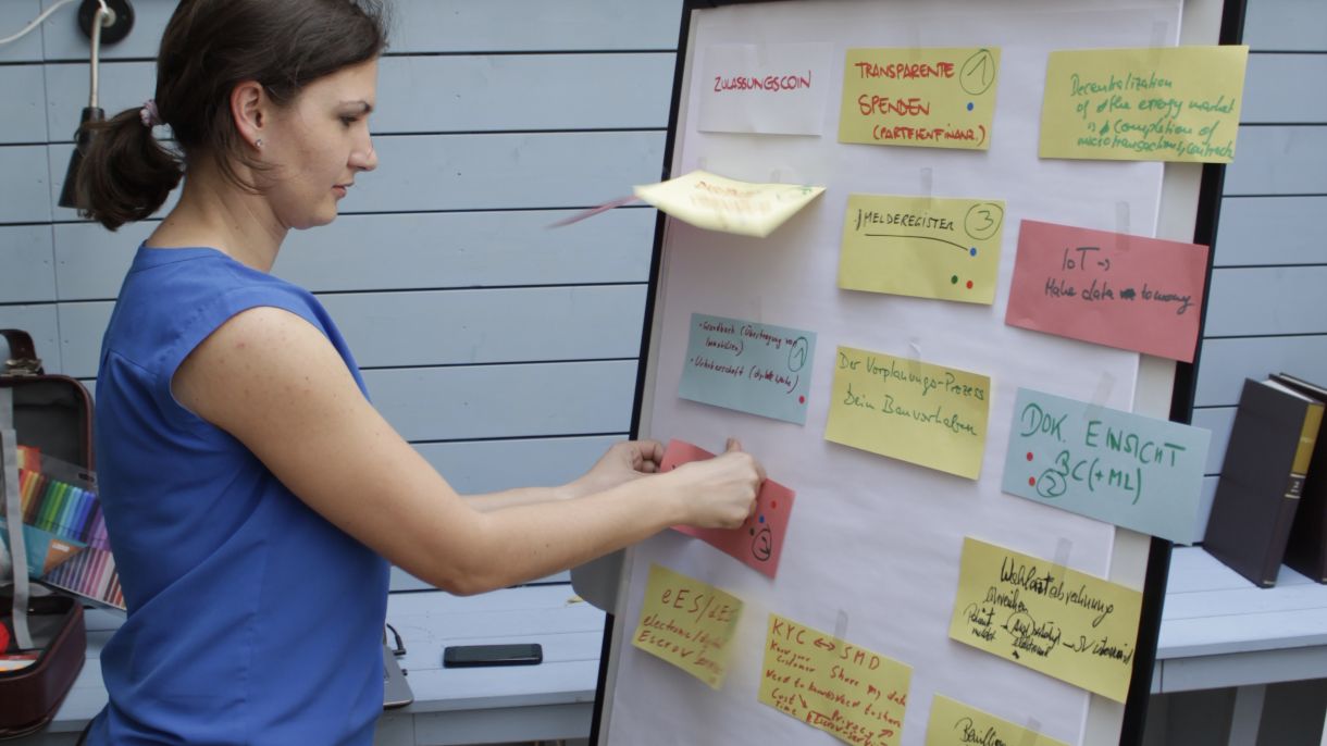 DIMCA-Workshop Blockchain, Frau steht vor Whiteboard mit Postits