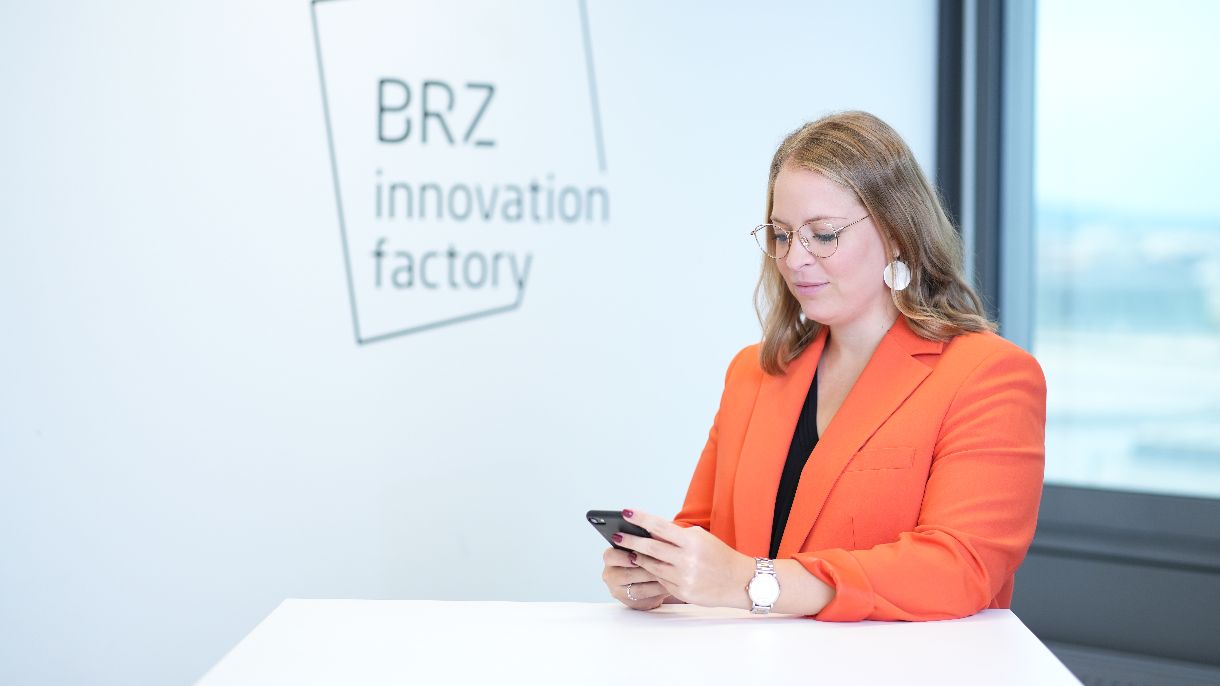 Dame in orangener Jacke schaut aufs Handy