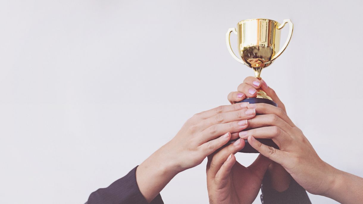 Hände von verschiedenen Personen halten gemeinsam einen Pokal