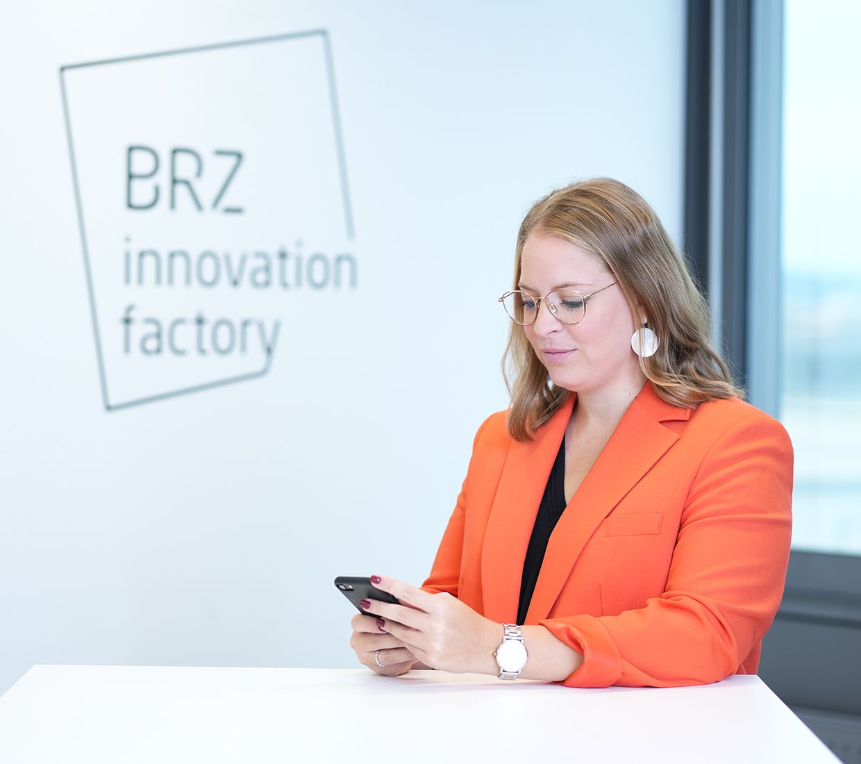 Dame in orangener Jacke schaut aufs Handy