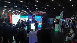 Foto von Standbesucherinnen und Standbesuchern der BRZ-Gaming Area auf der LEVEL UP Messe in Salzburg. Der BRZ-Messestand befindet sich in einer dunklen Veranstaltungshalle, der BRZ-Messestand sticht durch seine LED-Beleuchtung heraus. 