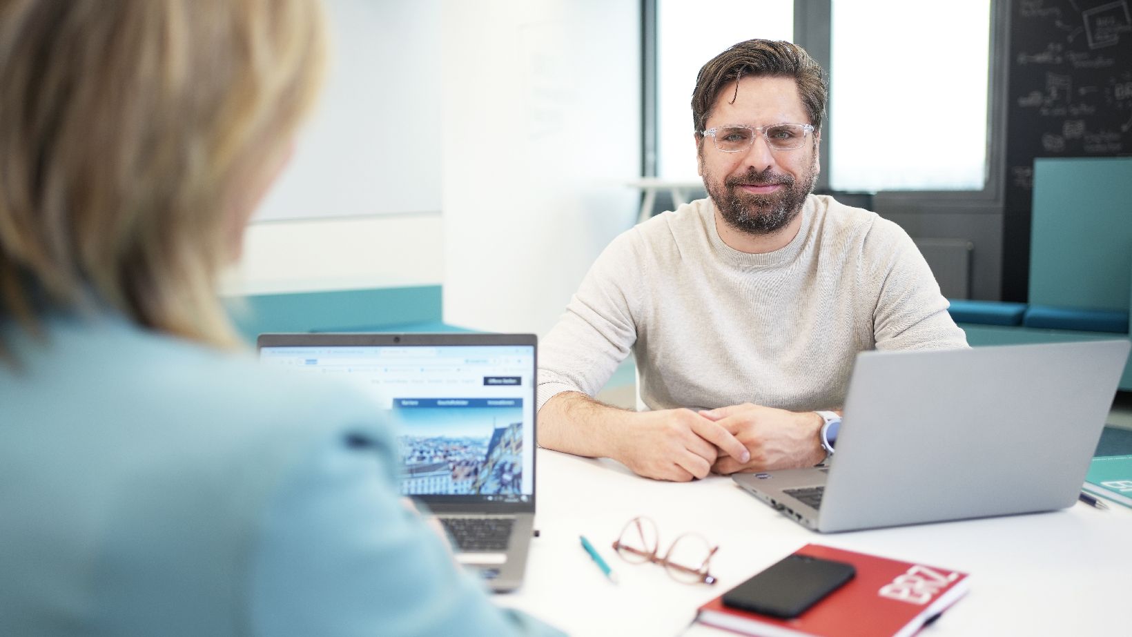 Mann mit Brille sitzt bei seinem Laptop und lächelt in die Kamera.