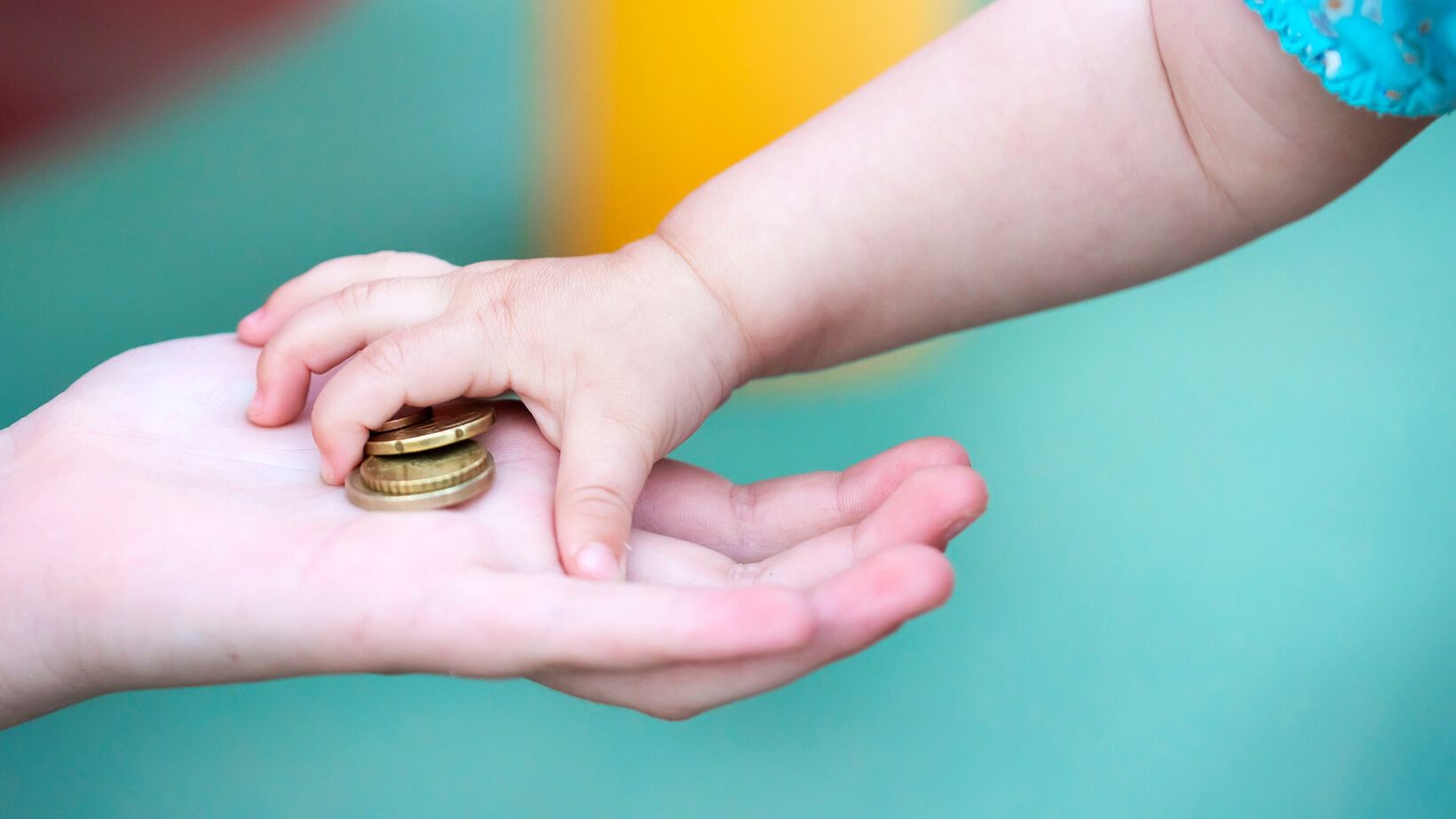 Die Hand eines Kleinkinds  greift nach Münzen in der Hand eines Erwachsenen
