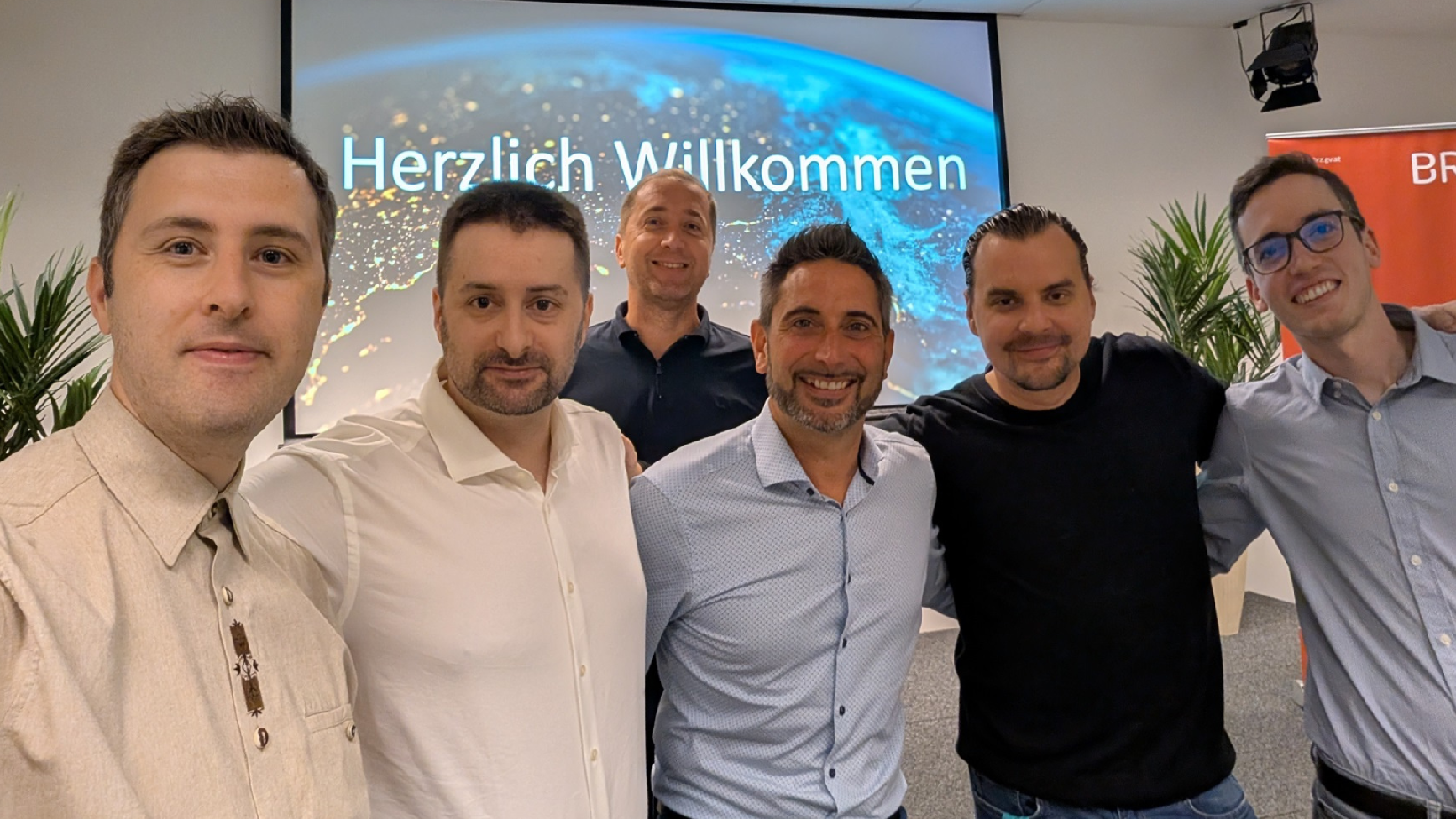 Eine Gruppe an Männern stehen Arm in Arm vor einer Leinwand