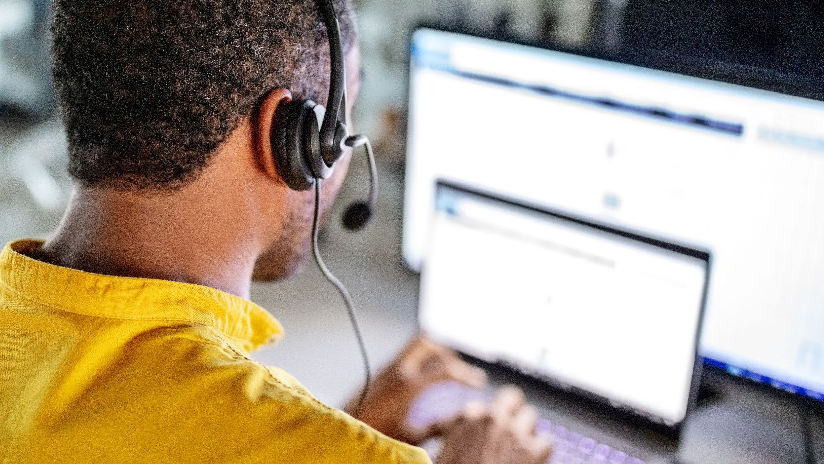 Service-Center Mitarbeiter von hinten mit Headset tippt am Laptop