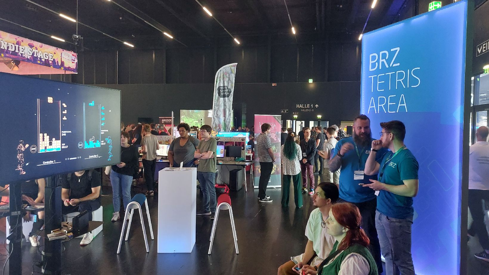 BRZ Tetris Area auf der LEVEL UP Gamingmesse. BRZ-Kollegen im Gespräch miteinander, Standbesucher:innen spielen Tetris und unterhalten sich.