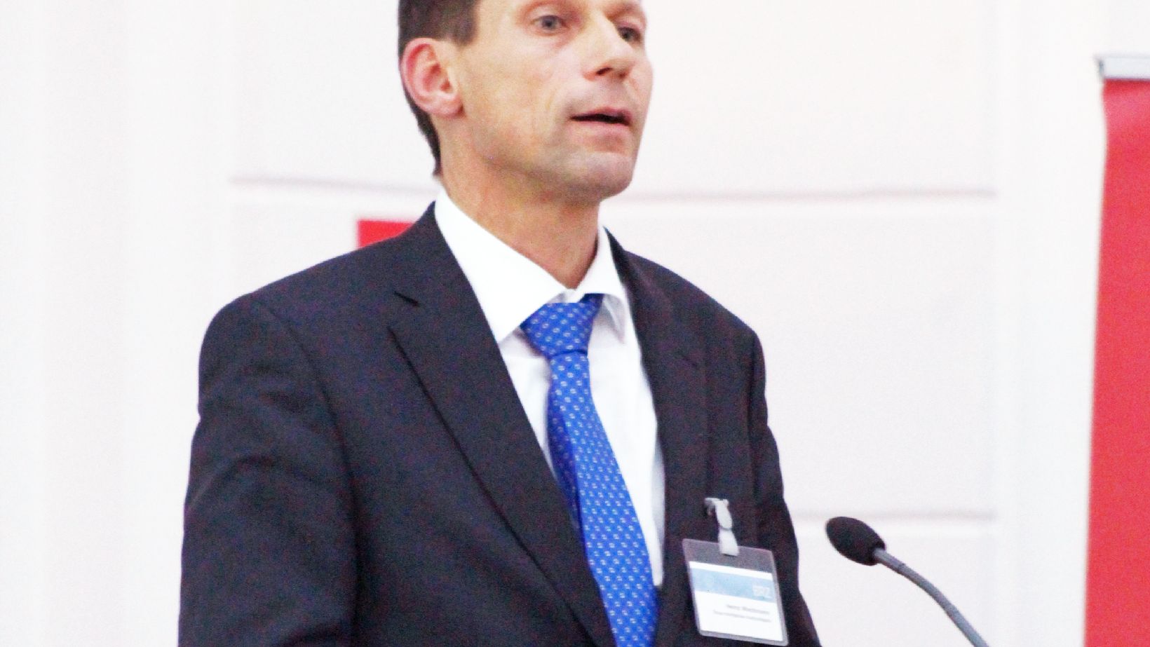 DIMCA Blockchain 4, @BRZ/Alexander Aigner Heinz Wachmann, im dunklen Anzug mit blauer Krawatte am Rednerpult