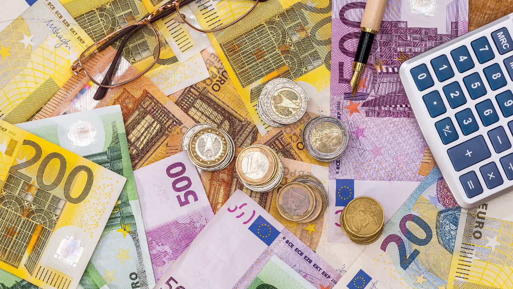 Euro Scheine und Münzen, sowie ein Stift, ein Taschenrechner und eine Brille.